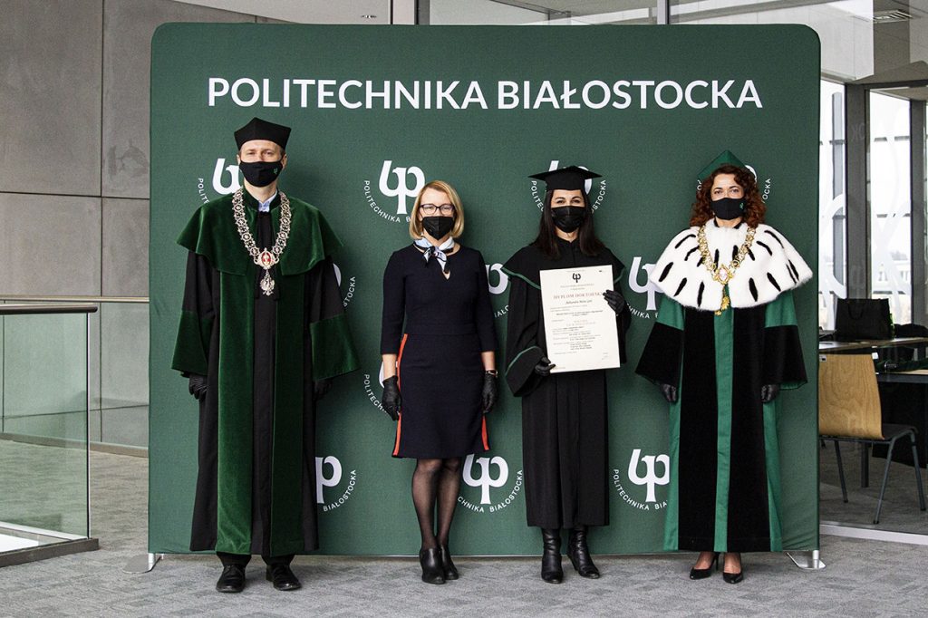 Święto Politechniki Białostockiej. Promocja doktorska dr Aleksandry Gulc. Zdjęcie na tle ścianki z logotypami Politechniki Białostockiej. Stoją od lewej: Prorektor ds. Nauki dr hab. inż. Marek Krętowski, prof. PB; Promotor Prof. dr hab. inż. Joanna Ejdys; dr Aleksandra Gulc; JM Rektor Politechniki Białostockiej dr hab. inż. Marta Kosior-Kazberuk, prof. PB