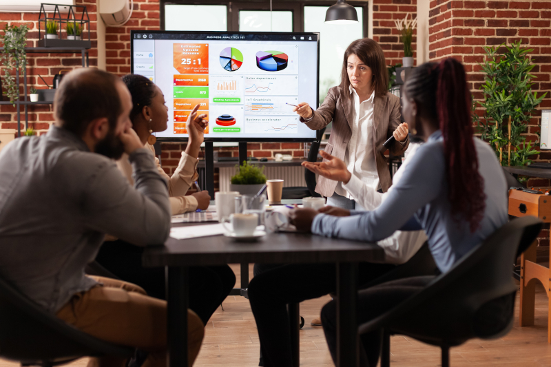 Businesswoman standing in front on monitor explaining management statistics